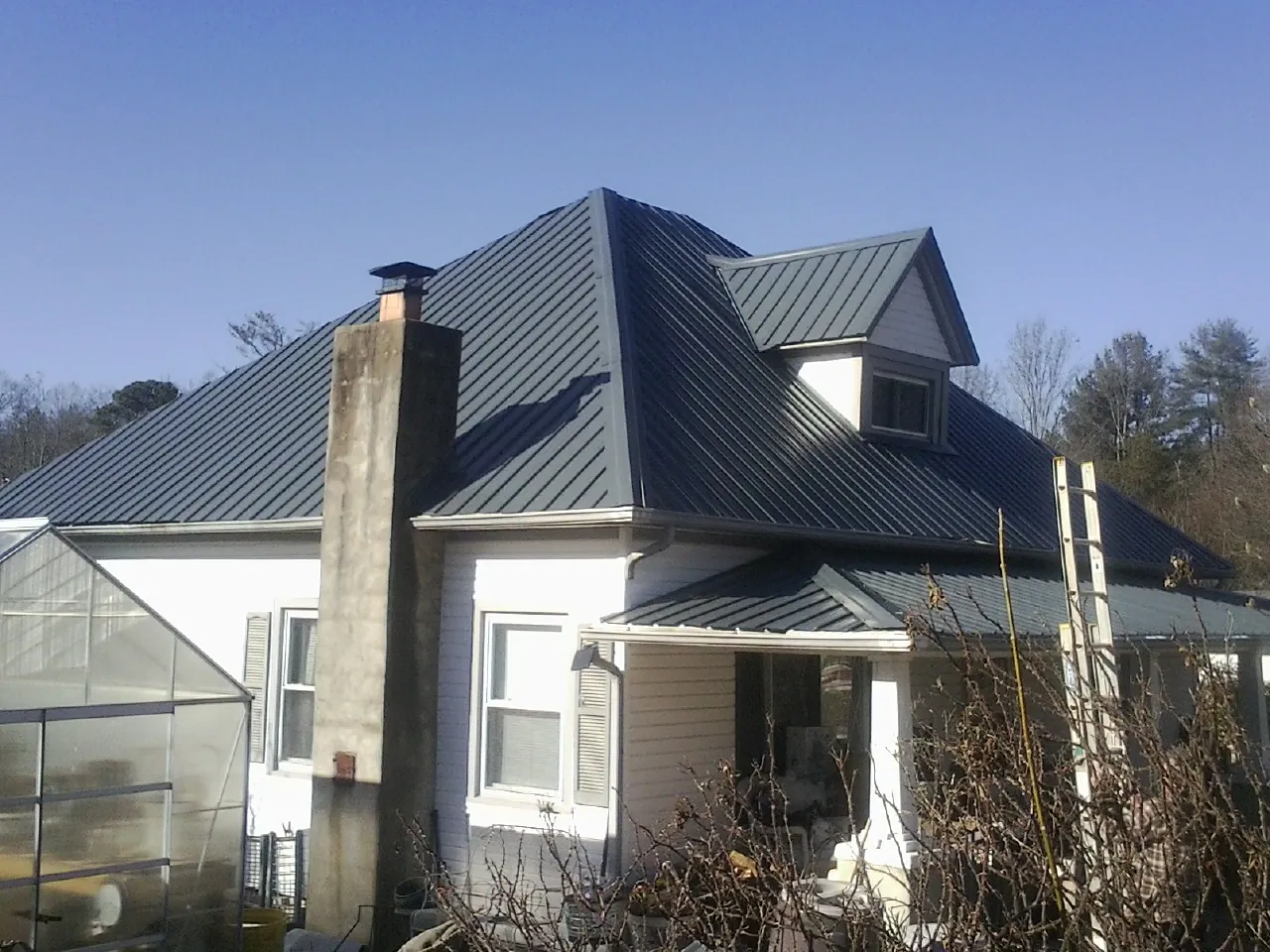 Dark blue standing seam metal roof on a white farmhouse with dormer — Slate & Tile Roof Repair by Roofing Brothers in Deltona