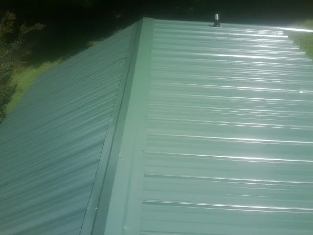 New green metal panels meeting at the ridge of a roof — Flat Roof Repair work by our crew in Deltona