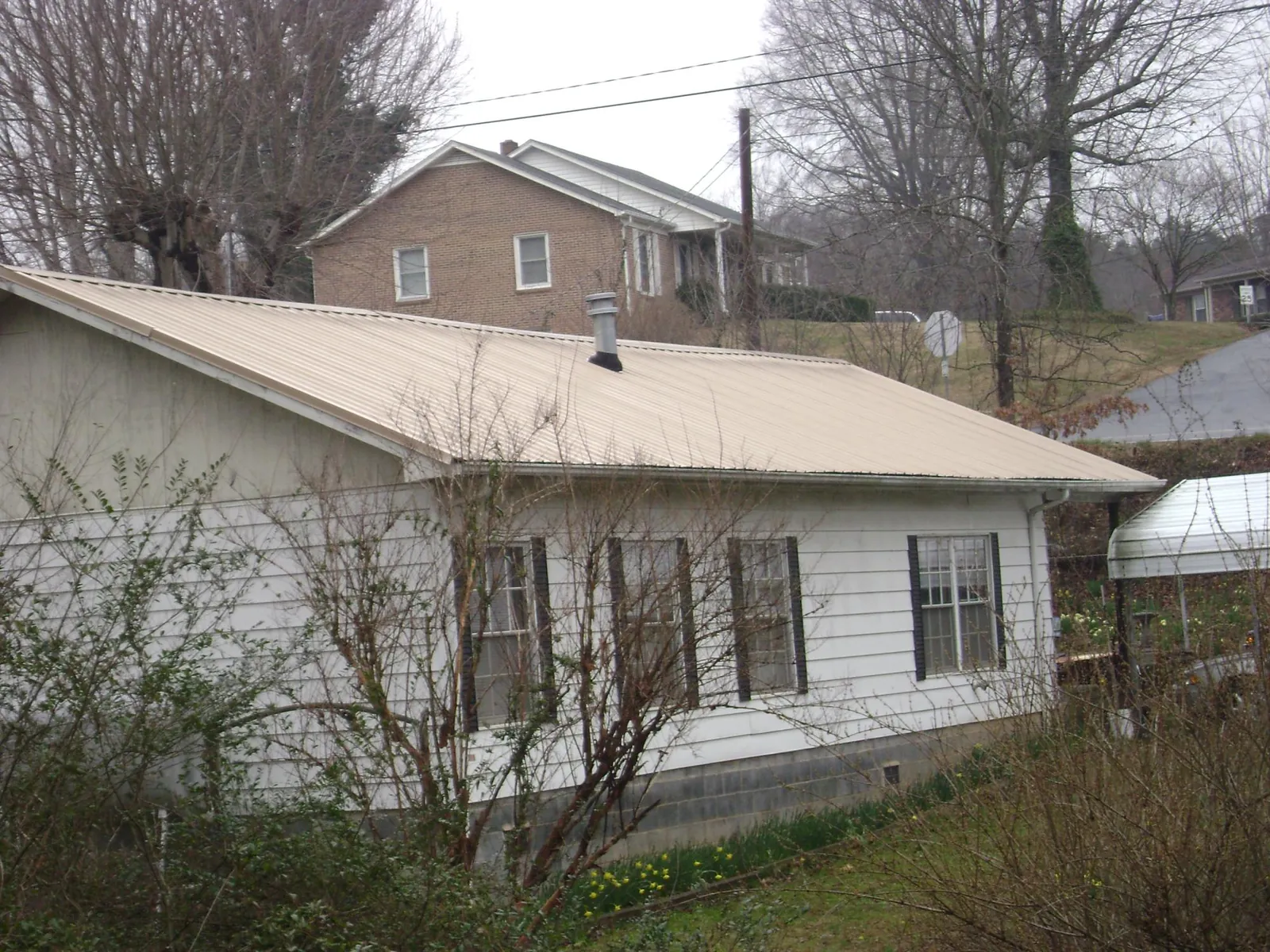 Tan metal roof on a white sided house set into a hillside — Commercial Roofing by Roofing Brothers in Deltona
